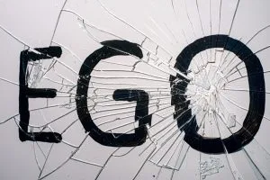 The word "EGO" is prominently displayed, fragmented by a spiderweb of cracks