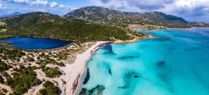 Turquoise waters gently lap against a sandy beach surrounded by lush hills
