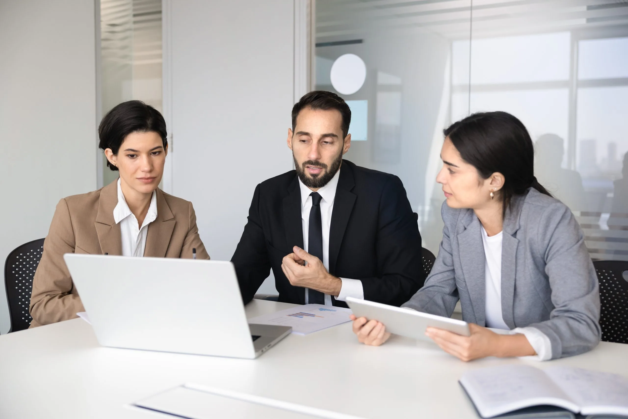 Three professionals engage in a discussion while reviewing a laptop at a conference table
